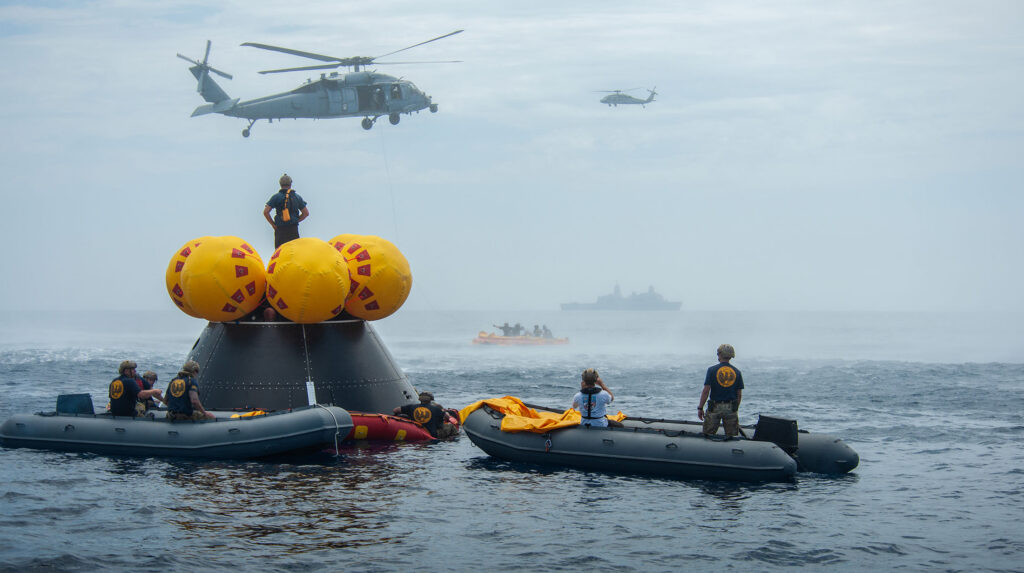 Naval helicopter pilots from Helicopter Sea Combat Squadron (HSC) 23 “Wildcards” fly over the Orion Crew Module Test Article (CMTA) with American flags after completing flight operations during an Artemis II mission simulation during NASA’s Underway Recovery Test 10 (URT-10) off the coast of San Diego.